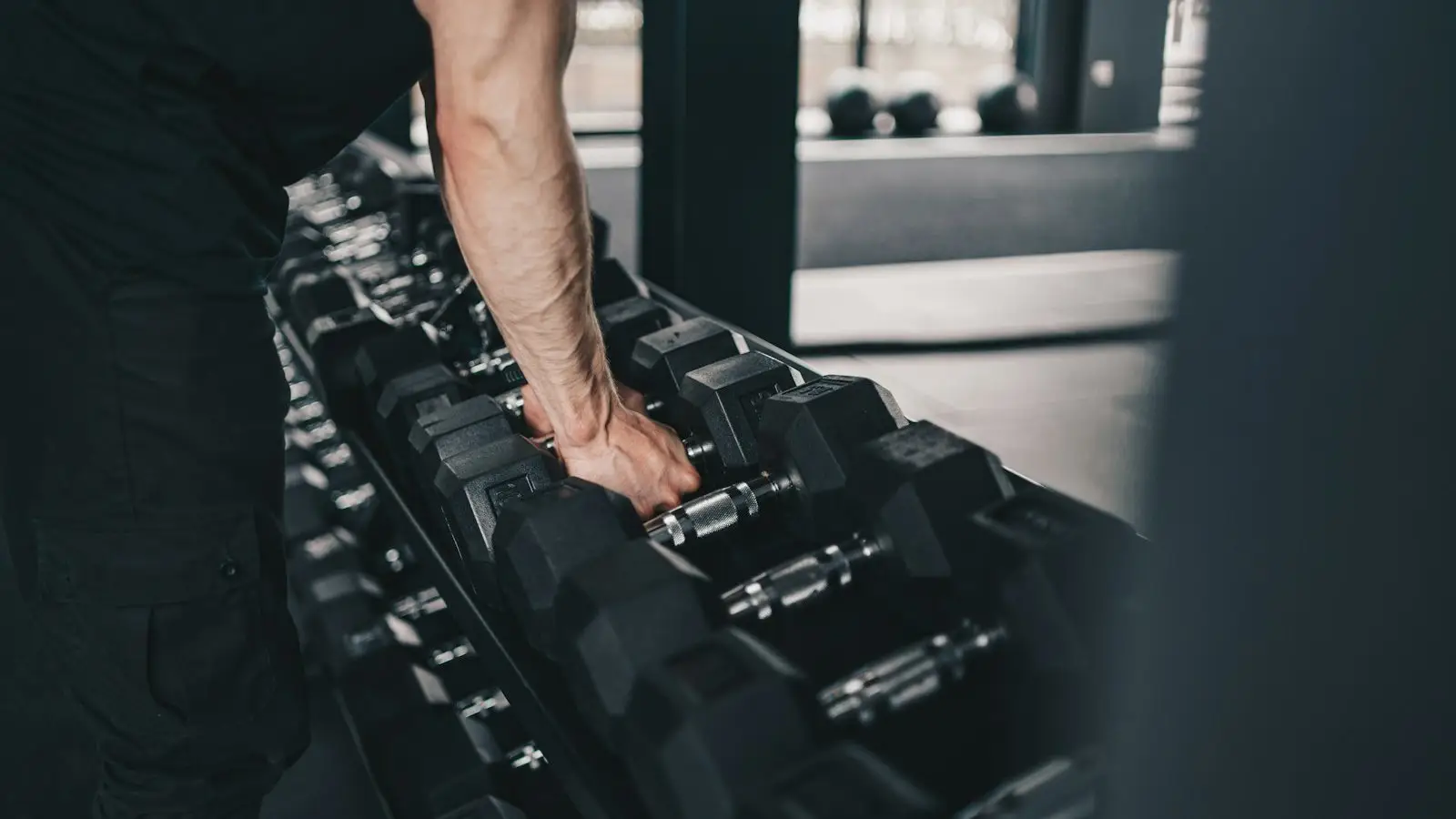 A man's arm reaching for a dumbbell on a rack in a quiet gym