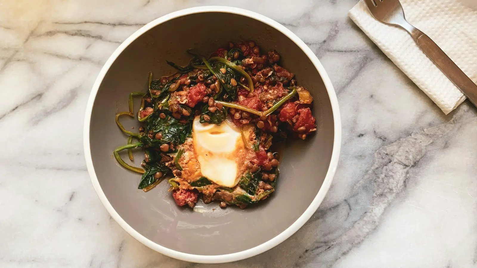 A bowl of lentils cooked with spinach and tomato, an iron rich meal, on a marble table